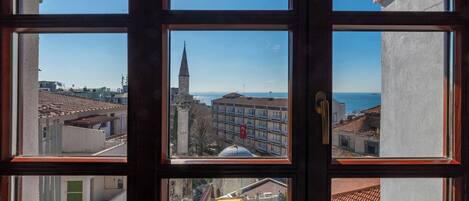 A view through a window with multiple panes, revealing a cityscape with buildings, a church spire, and a body of water.