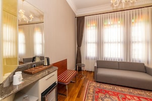 Habitación de hotel con un espejo grande, una mesita de noche de madera, un sofá, una pequeña mesa redonda y una alfombra estampada.