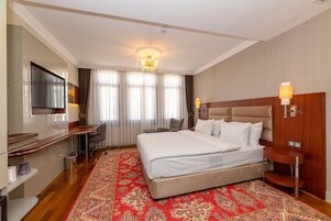 A hotel room with a large bed, a desk, a TV, and a chandelier.