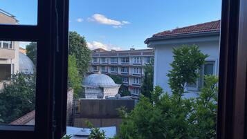 A view through a window of a building with a dome structure, a multi-story residential building, and some greenery.