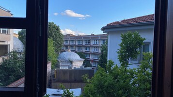 Vista attraverso una finestra che mostra un edificio con una struttura a cupola, un condominio a più piani e un po' di vegetazione.