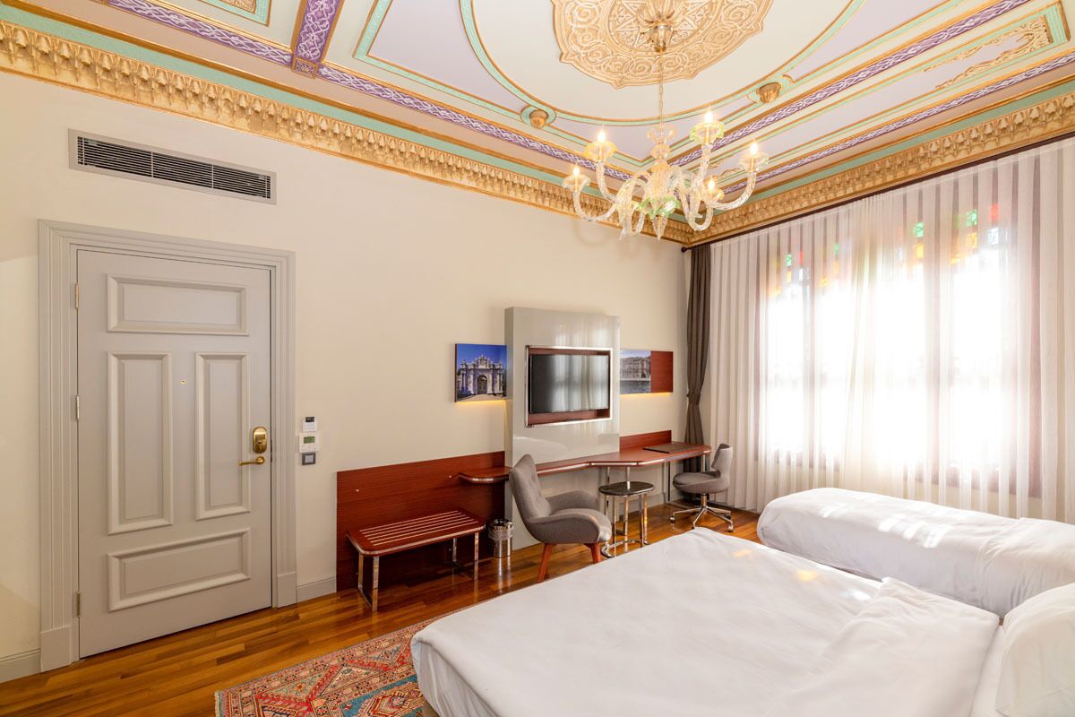 A hotel room with a large bed, a desk with a chair, a TV, and a window with curtains.