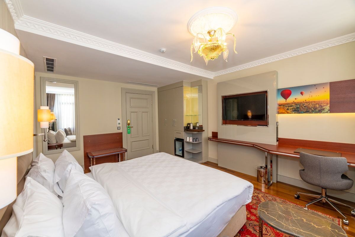 Een hotelkamer met een bed, een bureau, een stoel, een televisie en een schilderij aan de muur.