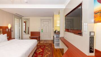 Quarto de hotel com cama, escrivaninha, espelho, televisão e painel de controle.