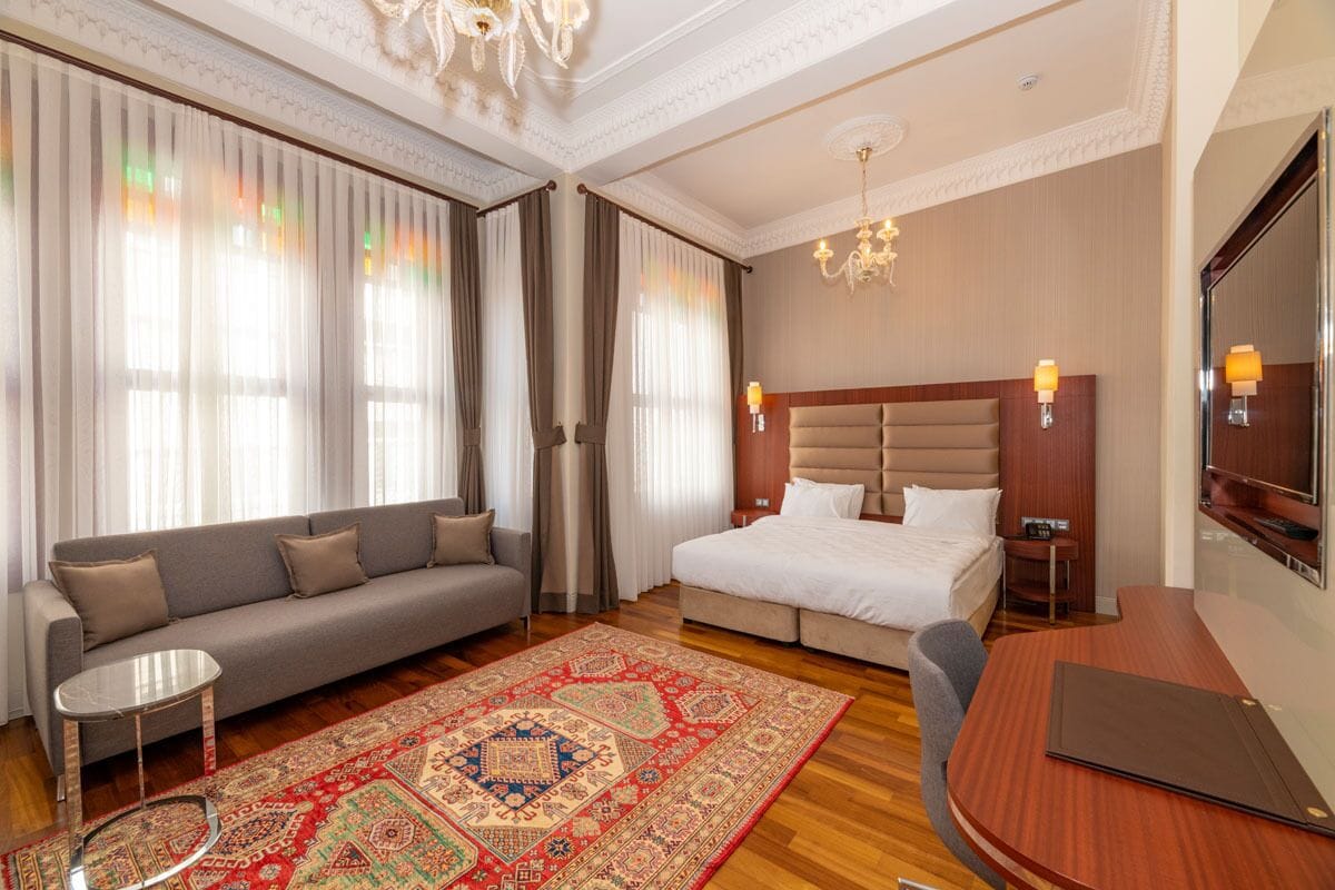 A hotel room with a sofa, bed, TV, and a decorative rug.