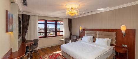 A hotel room with a large bed, a desk, a chair, a nightstand, and a view of the city through the window.