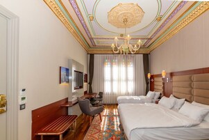 A hotel room with a large bed, a desk with a chair, a television, and a chandelier.