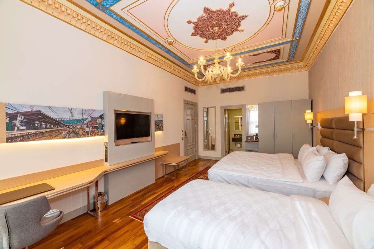 A hotel room with two beds, a TV, a desk, and a chandelier.