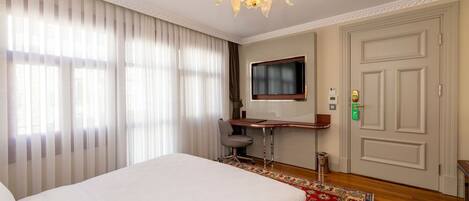 A hotel room with a large bed, a desk with a chair, a television, and a door with a lock.