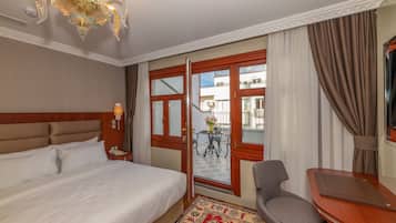 A hotel room with a large bed, a desk, a chair, a chandelier, and a view of the outside balcony.