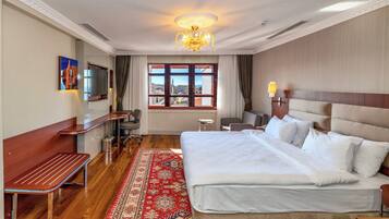 A hotel room with a large bed, a desk, a chair, a television, and a view of the city through the window.