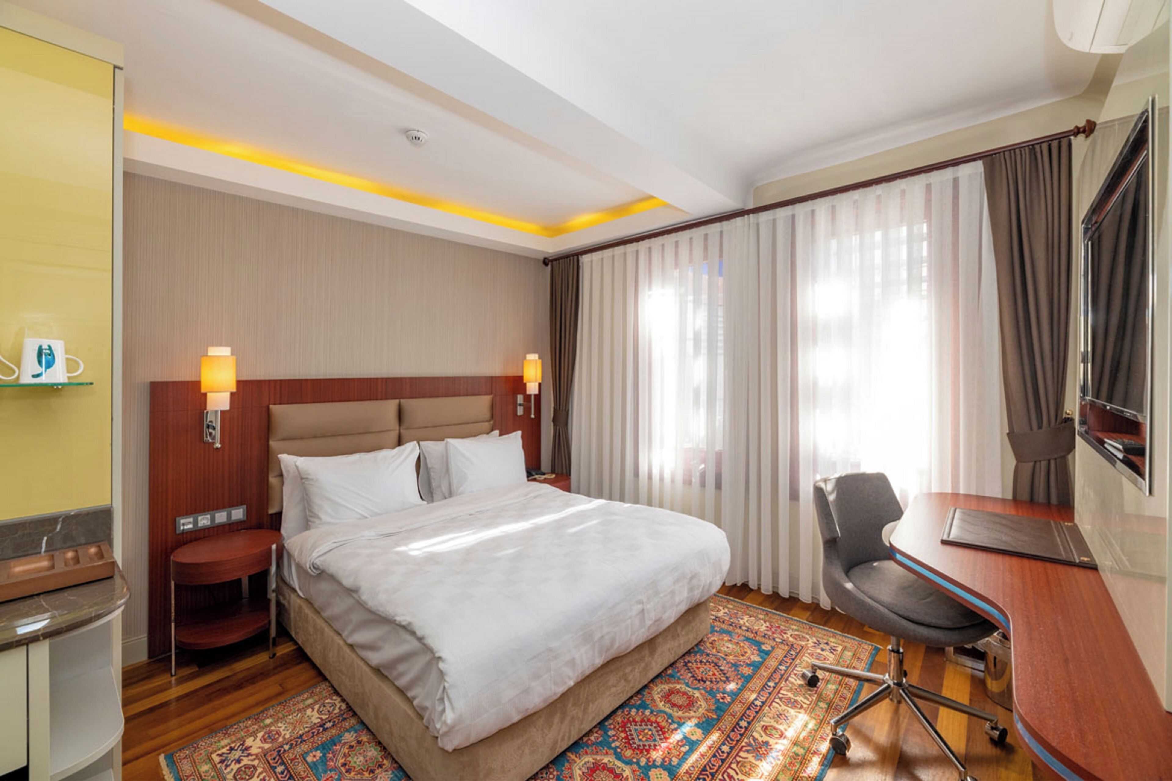 Una habitación de hotel con una cama grande, un escritorio, una silla, un televisor y una ventana con cortinas.