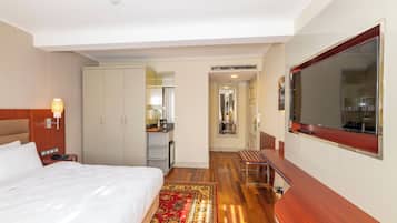 A hotel room with a bed, a desk, a TV, and a bathroom visible through an open door.
