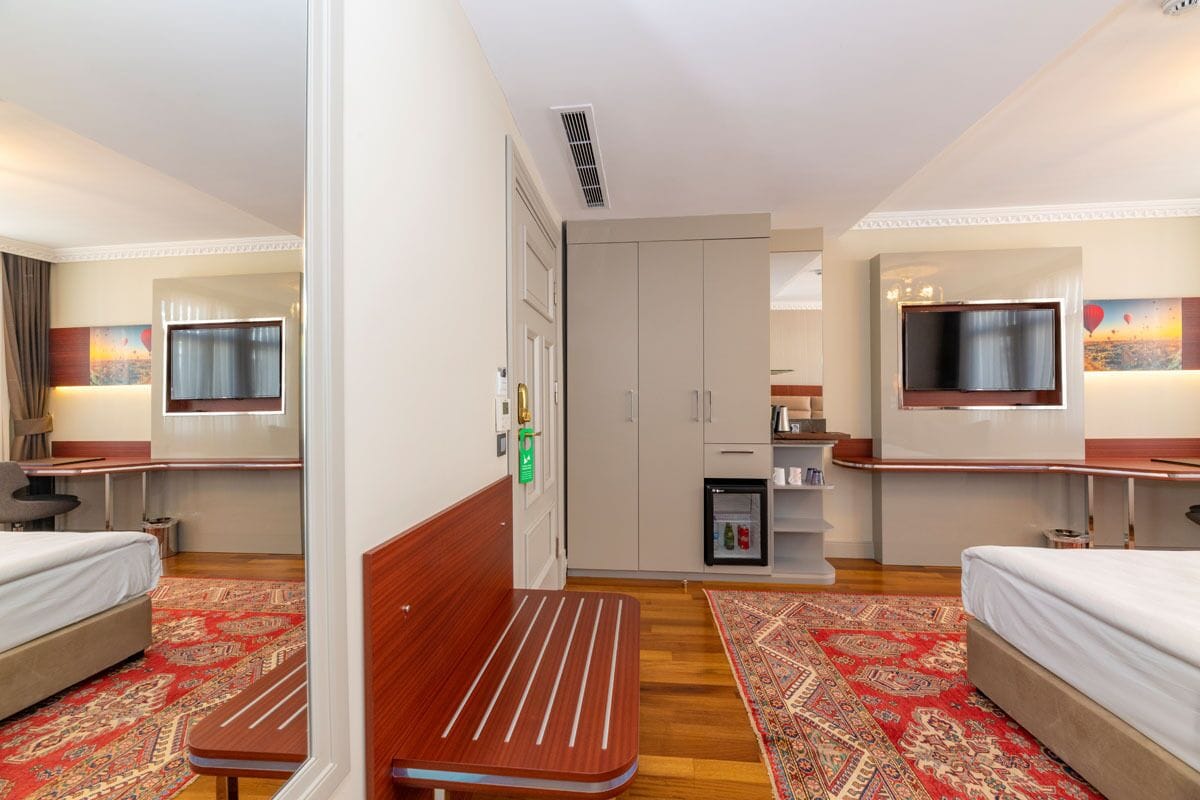 Een hotelkamer met twee bedden, een kitchenette, een televisie en een kleine koelkast.