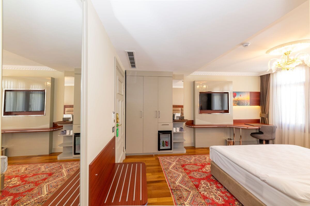 Habitación de hotel con cama, escritorio, silla, armario, televisión y refrigerador pequeño.