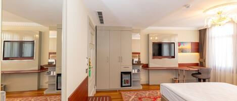 Habitación de hotel con cama, escritorio, silla, armario, televisión y refrigerador pequeño.
