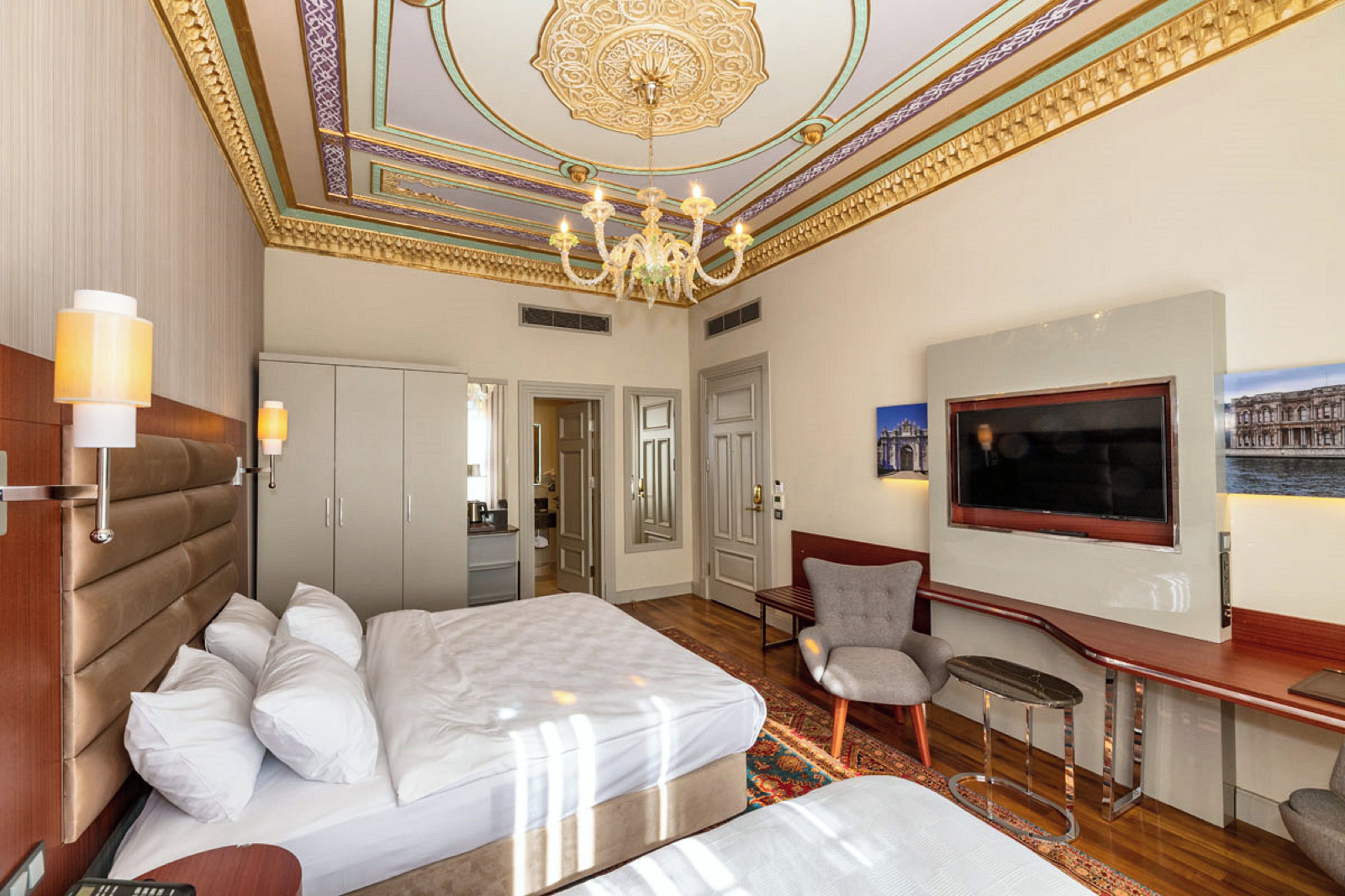 Une chambre d’hôtel avec un grand lit, une télévision, un bureau et un lustre.