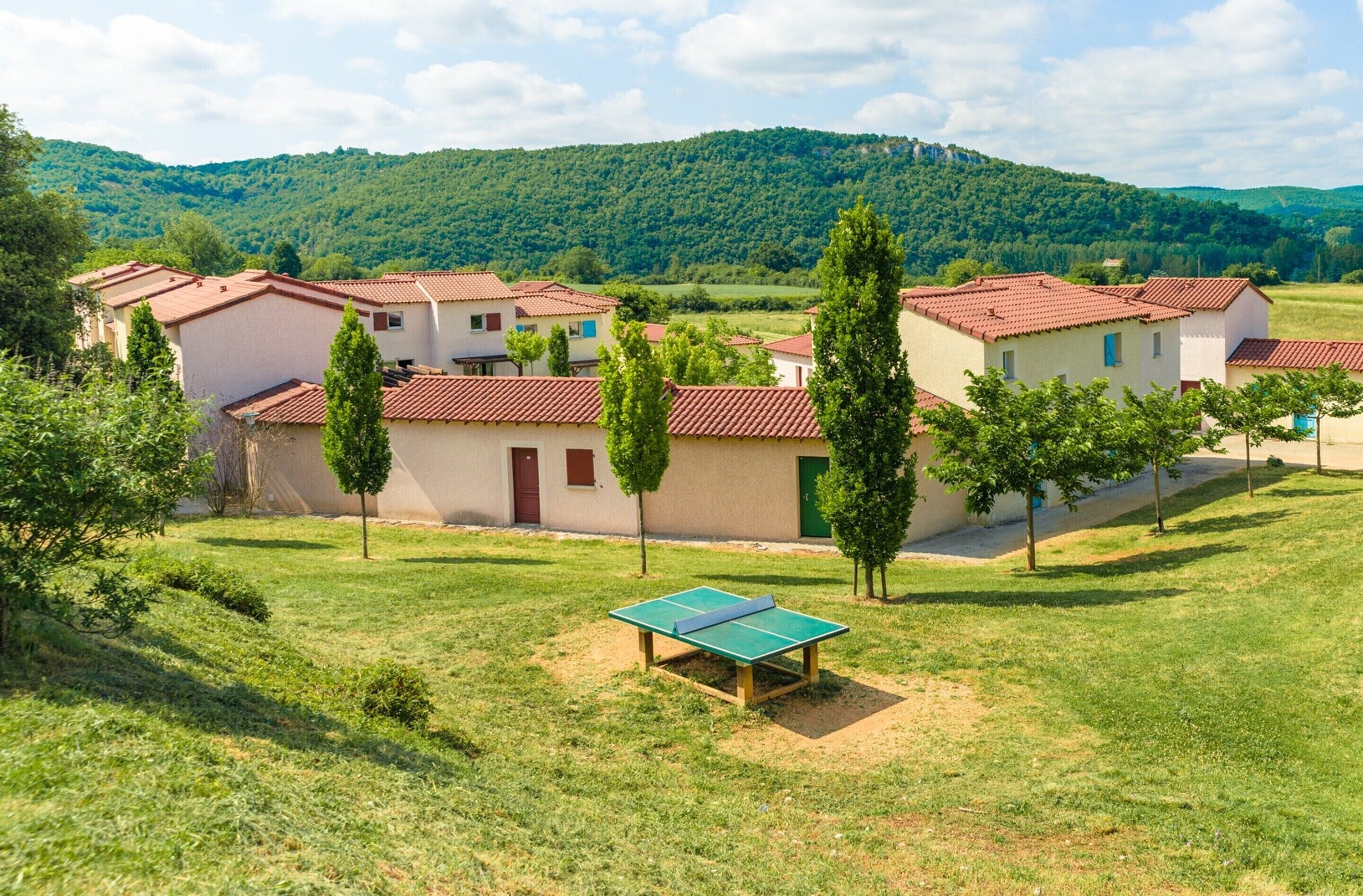 Un quartier résidentiel avec des maisons, une table de ping-pong et un paysage vallonné en arrière-plan.