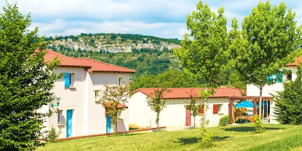 A row of white buildings with red roofs, a grassy area, and a mountain in the background.