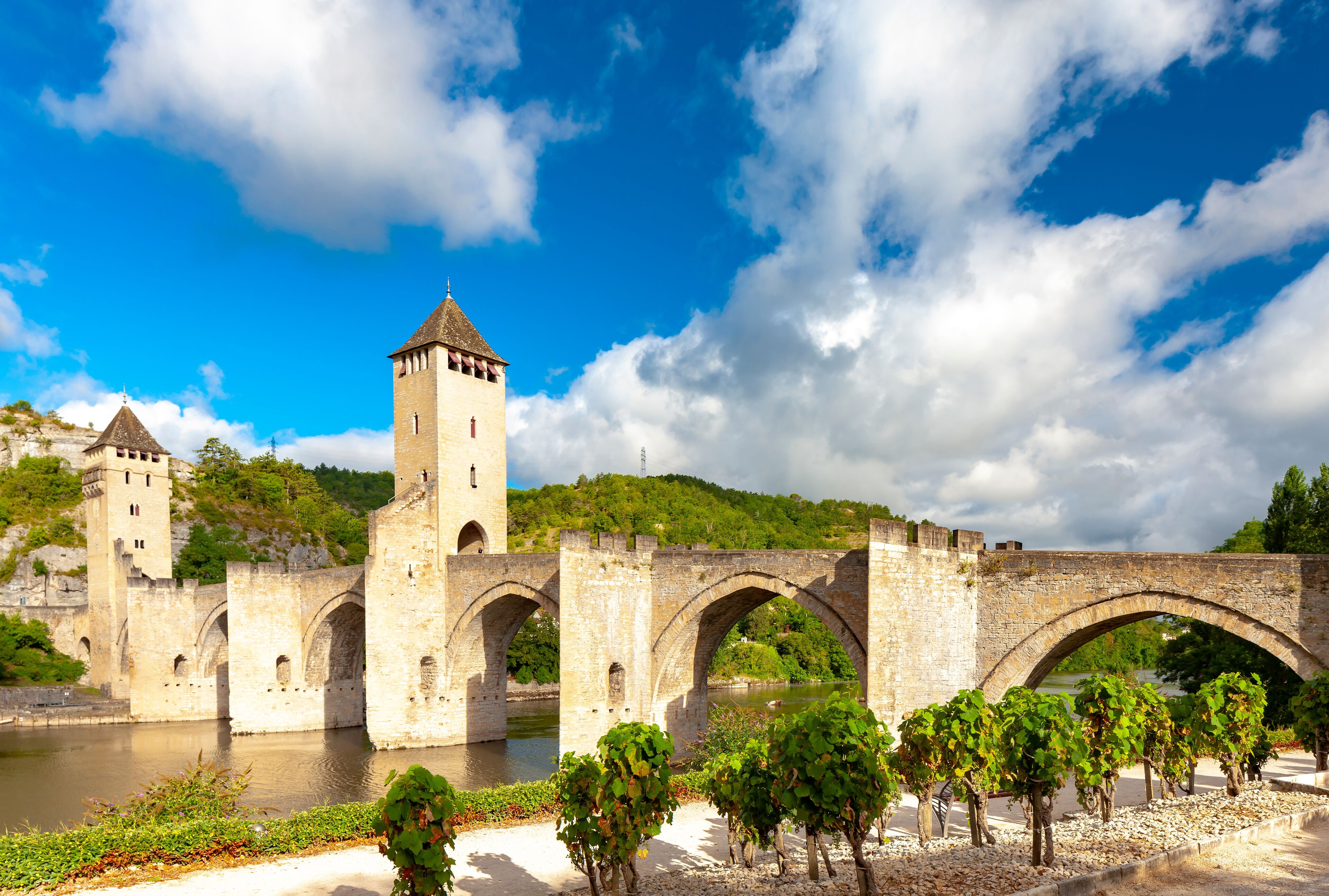 A historic stone bridge with arches over a river, a tower, and lush greenery.