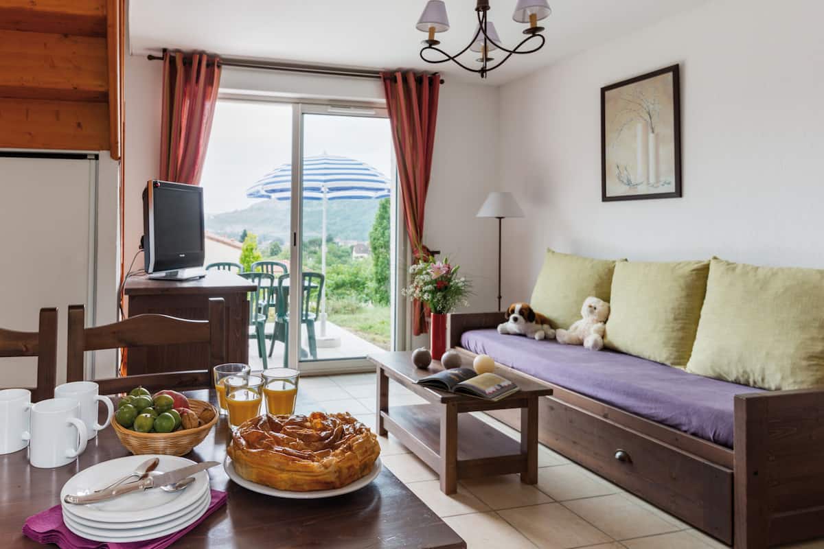 A cozy living room with a sofa, a dining table with breakfast items, a TV, and a view of the outdoors.