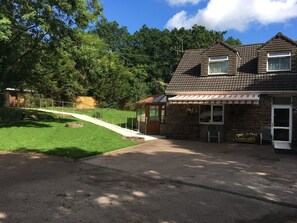 Une maison à deux étages avec un toit en pente, un petit porche doté d’une balustrade et une allée pavée menant à l’entrée.
