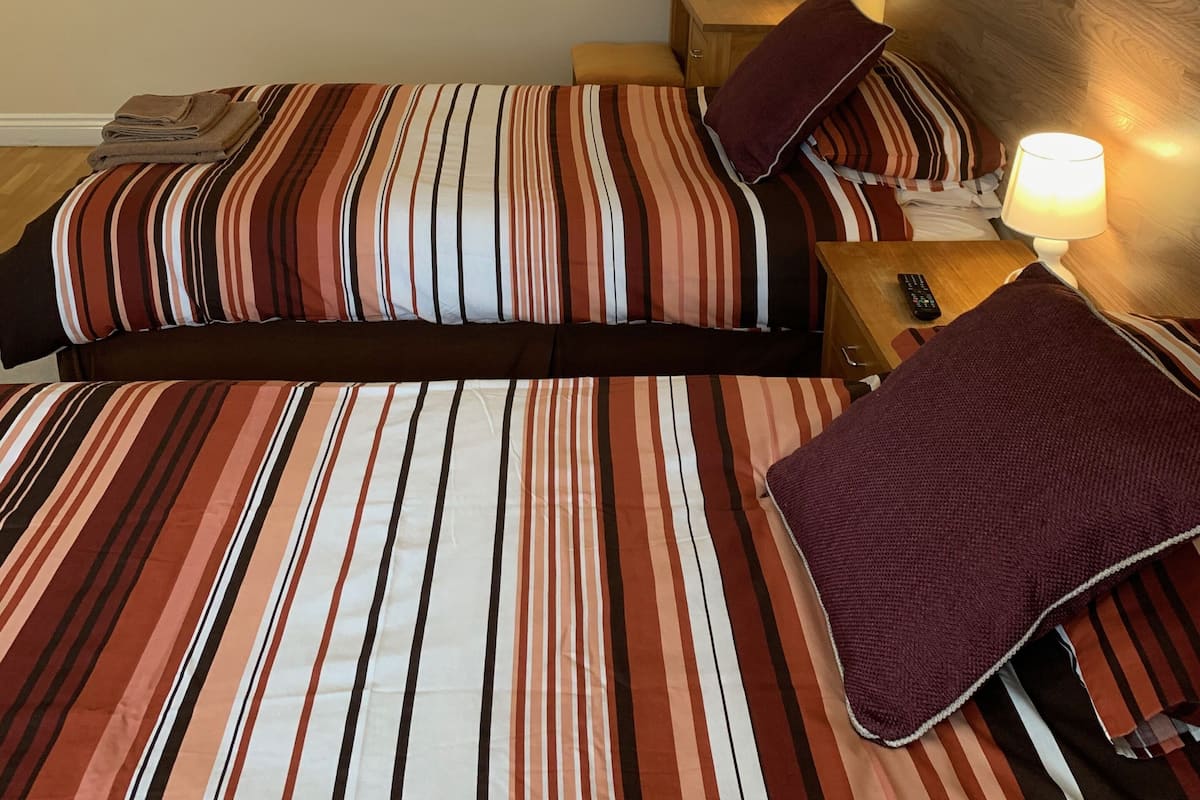 Ein Doppelbett mit gestreifter Bettwäsche, ein Nachttisch mit Lampe und ein wandmontierter Spiegel.