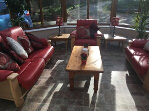 Une pièce baignée de lumière, avec des canapés en cuir rouge, une table basse en bois et deux petites tables d’appoint surmontées de lampes.