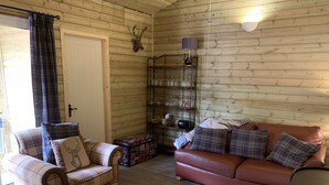 A cozy living room with a plaid armchair, a sofa, and a wooden wall with a mounted deer head. - BedrockLodge Buisness Centre HolidayLets (Bristol)