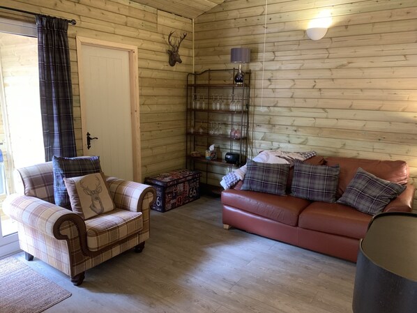 Un salon chaleureux avec un fauteuil à carreaux, un canapé et un mur en bois orné d’une tête de cerf.