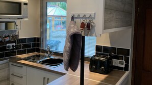 A modern kitchen with a microwave, toaster, and sink. A clock is mounted on the wall, and a towel hangs from a hook. - BedrockLodge Buisness Centre HolidayLets (Bristol)