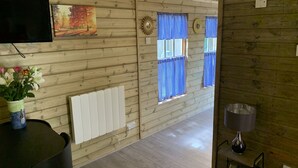 A wooden interior with a TV, a radiator, and a window with blue curtains. - BedrockLodge Buisness Centre HolidayLets (Bristol)