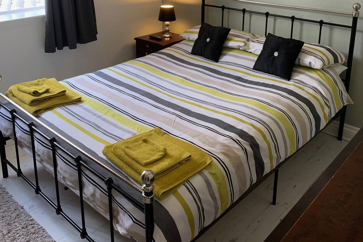 Ein ordentlich bezogenes Bett mit Streifenmuster, eine Nachttischlampe und ein an der Wand hängendes Bild von einem Reh.