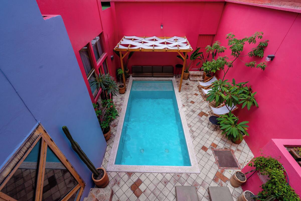 Ein kleiner Poolbereich mit einer Holzpergola, umgeben von Kübelpflanzen und einer rosafarbenen Mauer.