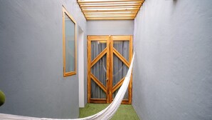 A narrow hallway with a hammock, a wooden door with curtains, and a green carpet. -  Hotel Boutique Casa de Arte (Oaxaca)
