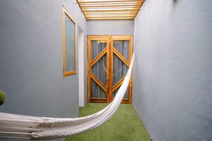 A narrow hallway with a hammock, a wooden door with curtains, and a green carpet.