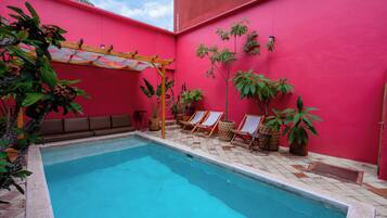 A swimming pool with a red wall, lounge chairs, and potted plants.