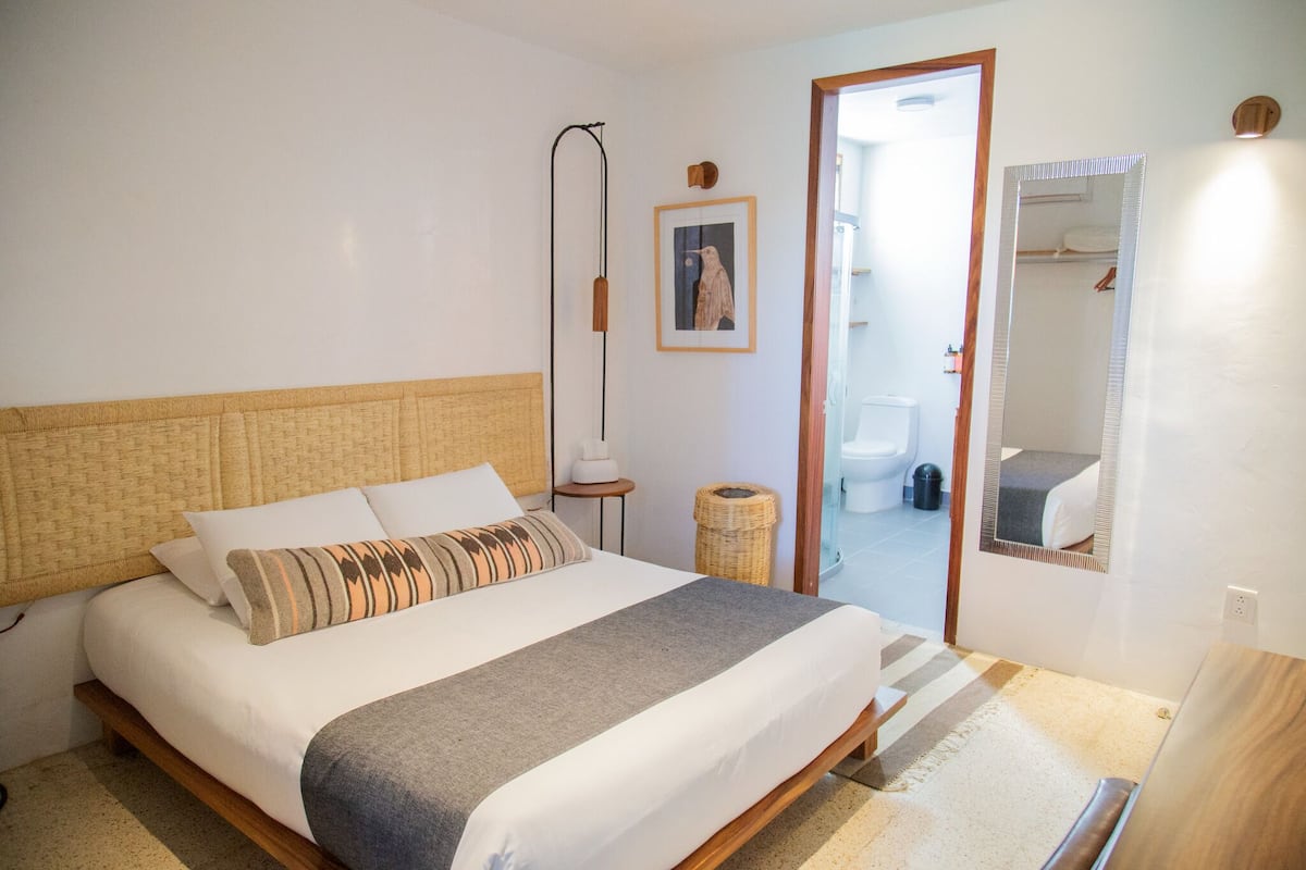 Ein Schlafzimmer mit einem Bett, einer Nachttischlampe, einem gerahmten Bild und einem Spiegel.
