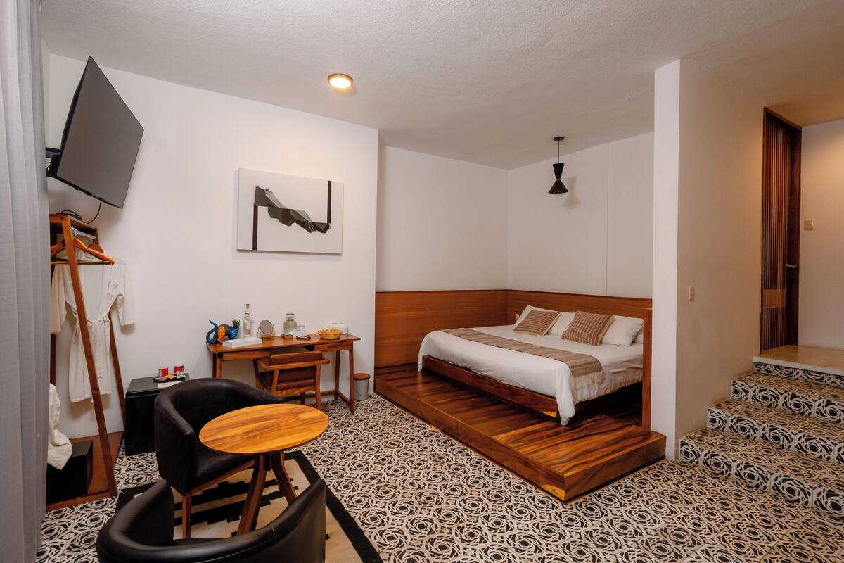 Ein kleines Hotelzimmer mit Bett, Schreibtisch, Stuhl, Fernseher und einem gestreiften Boden.
