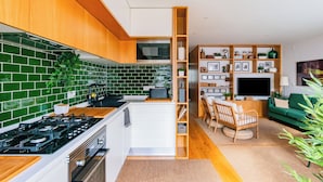A modern kitchen with green tiles, wooden cabinets, and a built-in microwave. - ShôLubi - Charming Quiet & Cozy (Lisbon)