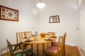 Un coin repas avec une table ronde en bois, des chaises et un saladier rempli de fruits.