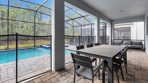 A covered patio with a pool, outdoor seating, and a view of the surrounding forest. - Movie Theater! Private Pool Oasis! Resort Near Disney! 2707 (Kissimmee)