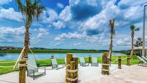 A serene outdoor area with a lake, lounge chairs, and palm trees. - Movie Theater! Private Pool Oasis! Resort Near Disney! 2707 (Kissimmee)