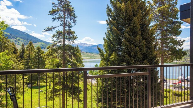Un balcón con vista a un lago, rodeado de árboles y montañas.