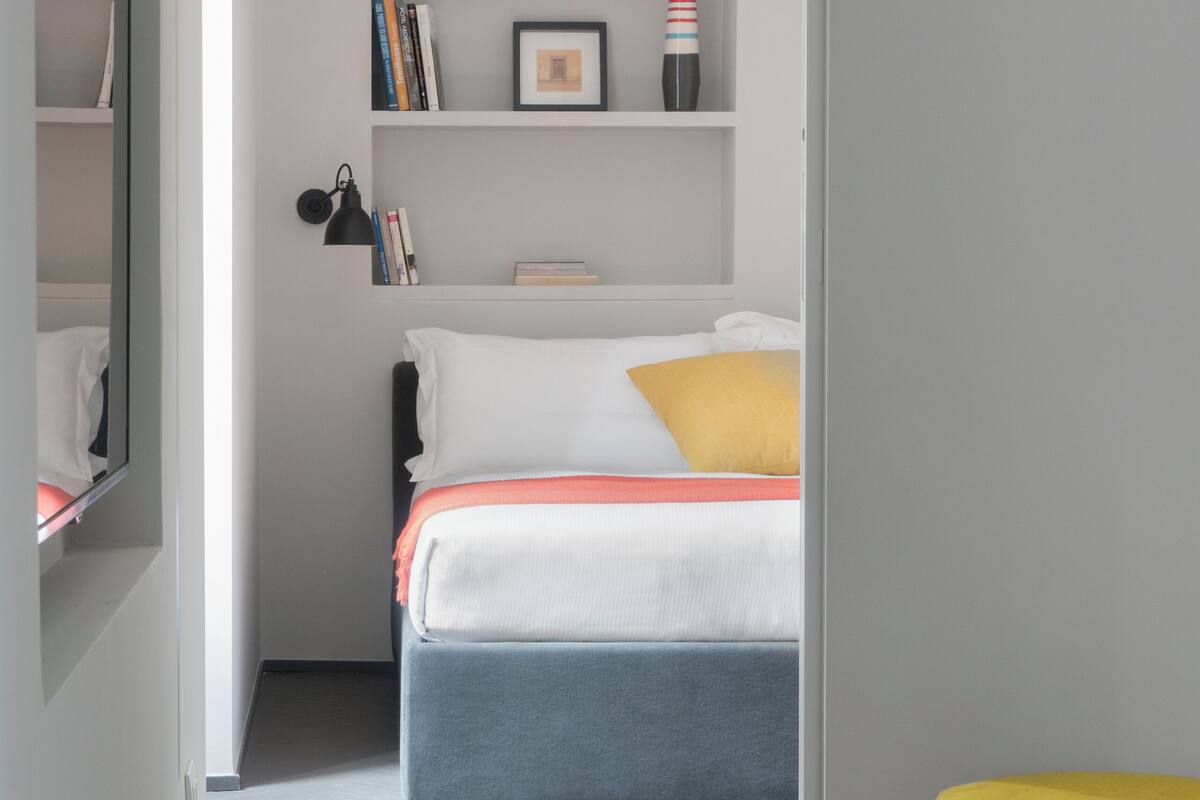 Ein modernes Schlafzimmer mit Bett, Nachttischen, einem Bücherregal und einem Spiegel.