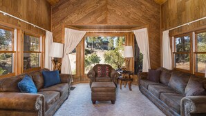 A log cabin interior with leather sofas, a central ottoman, and large windows offering a view of the outdoors. - Tree Haven (Yosemite National)