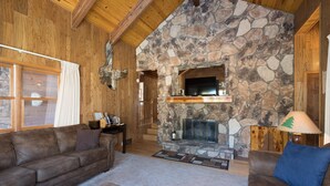 A cozy living room with a stone fireplace, wooden beams, and leather sofas. - Tree Haven (Yosemite National)