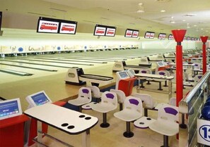 A bowling alley with lanes, bowling balls, and multiple bowling tables with chairs.