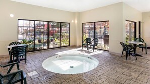 Un amplio espacio interior con una piscina central de fondo transparente, rodeado de sillas y mesas.