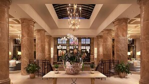 A lobby with marble columns, a chandelier, and a large table with potted plants.